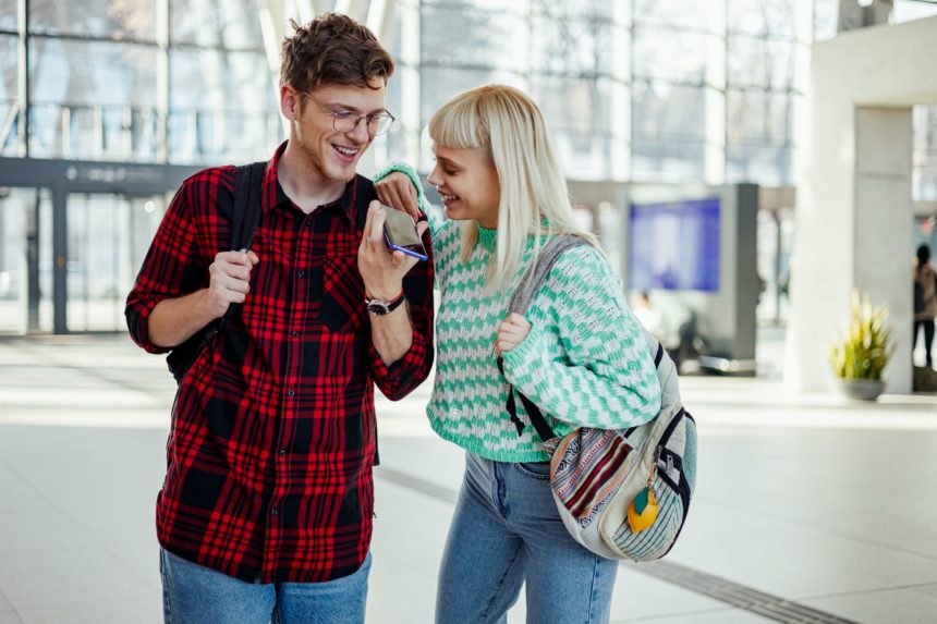 A young couple is using cellphone for communications at train station.