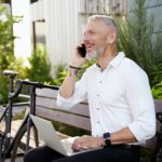 Establishing links. Modern middle aged businessman in white shirt talking on the phone, working on