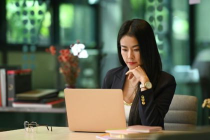 Focused millennial woman entrepreneur reading business information on her laptop computer.