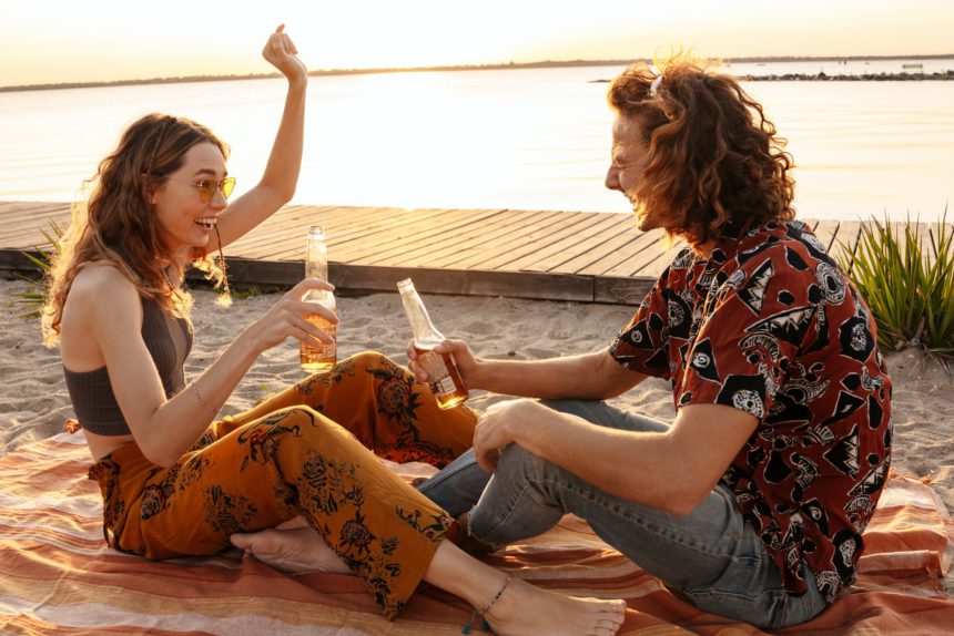 Positive young loving couple drinking beer at the beach